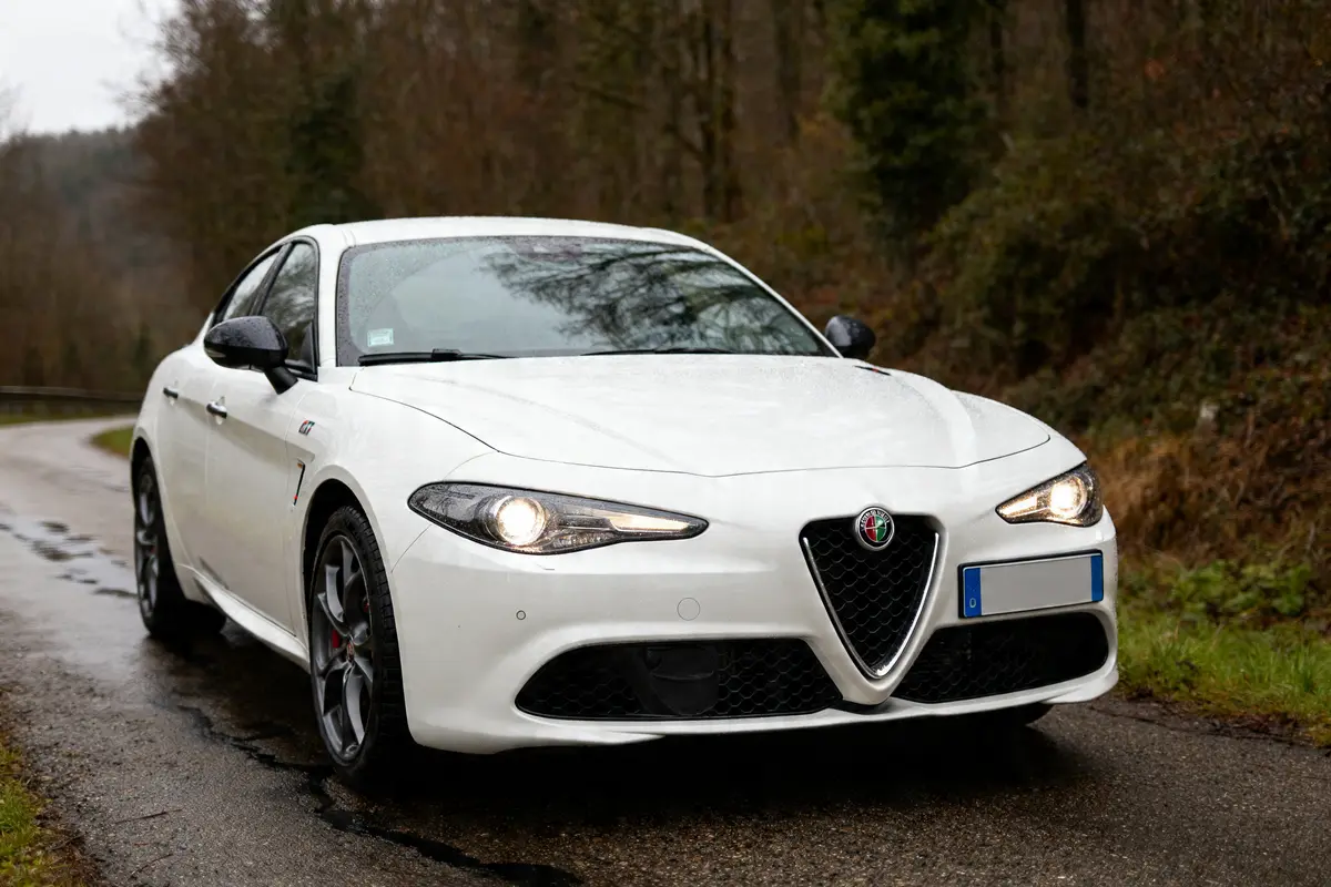 Voiture blanche Alfa Romeo Giulia GTA sur route de campagne humide et sinueuse