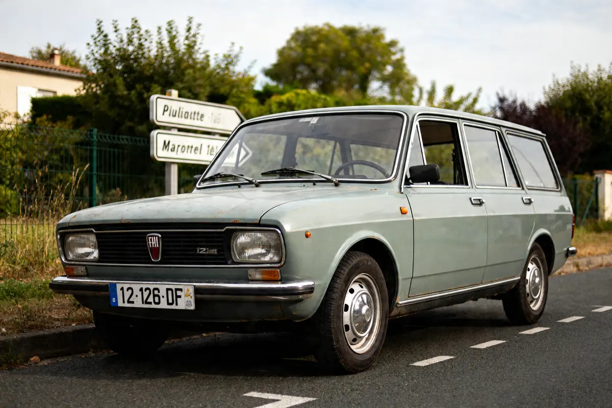 Fiat 128 Wagon vert stationné en bord de route avec panneaux en arrière-plan